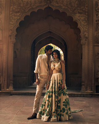 An ivory and green floral print lehenga, featuring intricate hand-embroidery in aari, zardozi and sequins. It is paired with a signature cut printed and hand-embroidered blouse in floral inspired motifs. The look is complete with a delicate floral printed organza dupatta with double scallop embroidered borders.